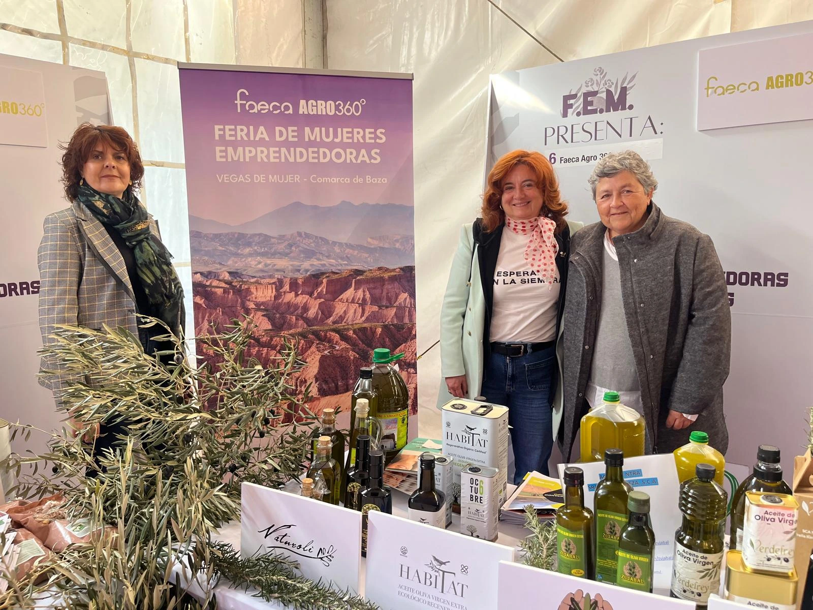 Tres mujeres en el stand de FAECA durante la Feria de Mujeres Emprendedoras mostrando marcas de aceite de oliva virgen extra local.